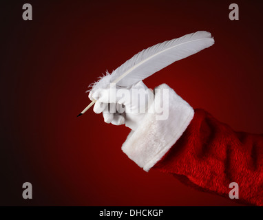 Closeup of Santa Claus holding a quill pen. Horizontal format on a light to dark red spot background. Stock Photo