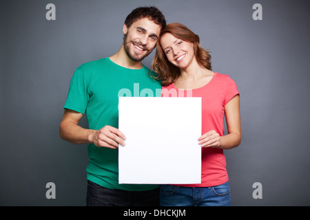 Portrait of young couple holding blank paper and looking at camera Stock Photo