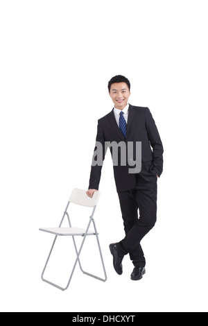 Portrait of young businessman standing near chair,relaxing Stock Photo