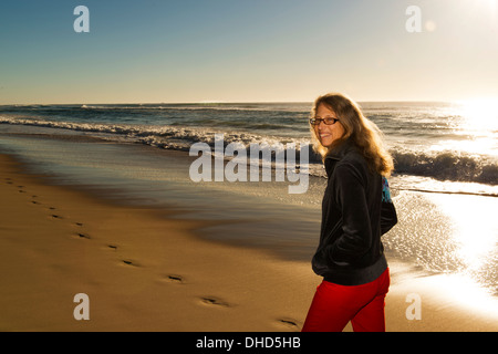 Blond mature woman walking on beach at sunrise. Stock Photo