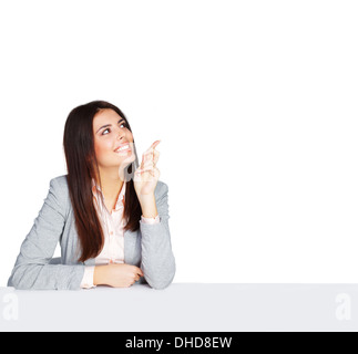 Young happy businesswoman sitting at the table and pointing up at copyspace Stock Photo