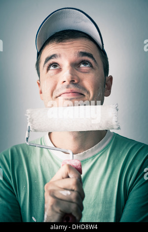 Thoughtful smiling creative man with paint roller looking up. Stock Photo