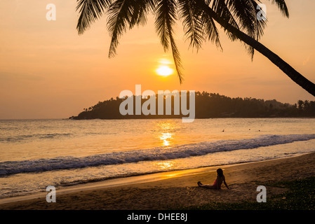 Woman sitting on Mirissa Beach watching the sun set, South Coast of Sri Lanka, Southern Province, Sri Lanka, Asia Stock Photo