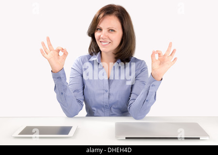 Business woman is sitting in front of a laptop and a tablet computer and showing double ok gesture Stock Photo
