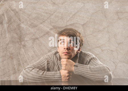 Pensive young man in gray pullover over gray background Stock Photo