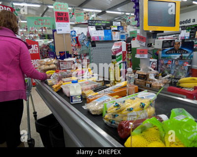 Woman rear back of shopper at checkout counter filled with groceries food in plastic packaging at Co-Op supermarket in Wales Britain UK  KATHY DEWITT Stock Photo