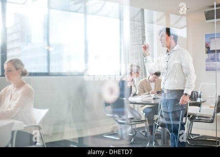 Man writing on glass wall, colleagues in background Stock Photo