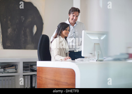 Businesswoman sitting at desk using computer, man behind her Stock Photo