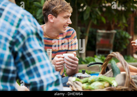 Friends sitting in garden with basket of fresh vegetables Stock Photo