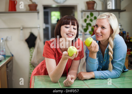 Two young women in kitchen holding apples