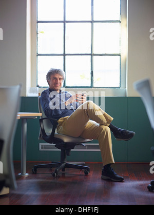 Mature businessman sitting on office chair wit cell phone Stock Photo