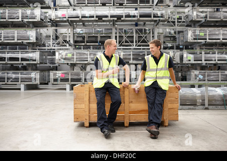 Two warehouse workers leaning on crate in engineering warehouse Stock Photo