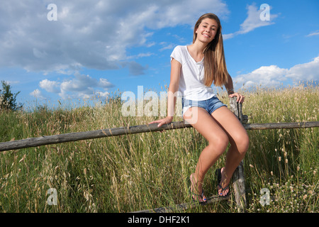 Teenage girl sitting on wooden fence, Tuscany, Italy Stock Photo