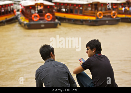 Two men sit on the bank of the Singapore River at Clarke Quay. Stock Photo