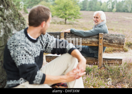 Senior man sitting on bench talking to mid adult man Stock Photo