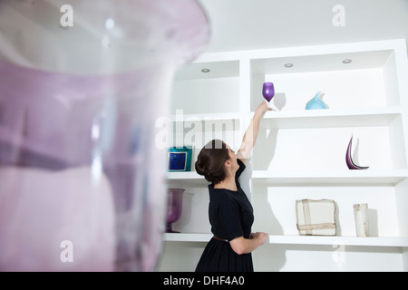 Young woman reaching for wine glass on shelf in living room Stock Photo