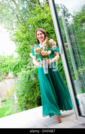 Young woman wearing green dress holding vase of flowers Stock Photo