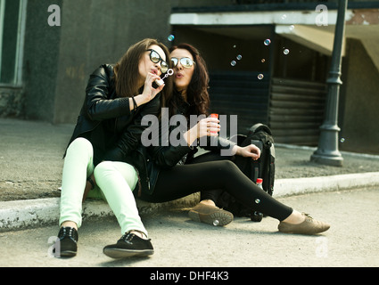 Two young woman blowing bubbles on street