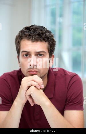 Young man resting chin on clasped hands Stock Photo