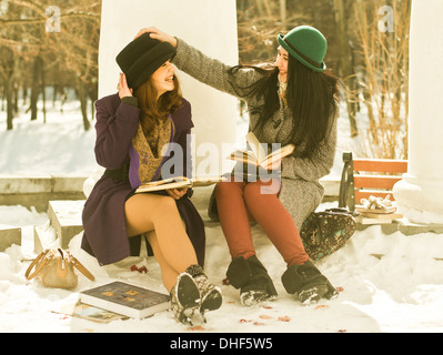 Two young women with books on park bench in snow Stock Photo