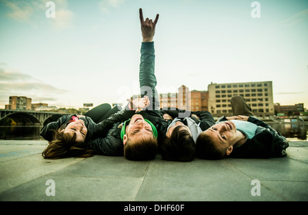 Four freinds lying on backs, one making rock and roll sign, Russia Stock Photo