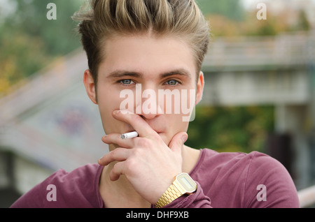 Attractive blue eyed, blond young man smoking cigarette outdoors Stock Photo