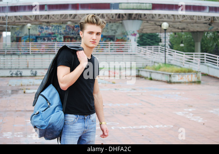 Handsome blond, blue eyed young man outdoors with ruck sack on shoulder, t-shirt and jeans Stock Photo