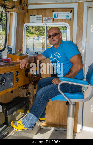 Captain of the Molly Bawn tour boat sits inside at the captain's chair of the boat in Mobile, Newfoundland, Canada. Stock Photo