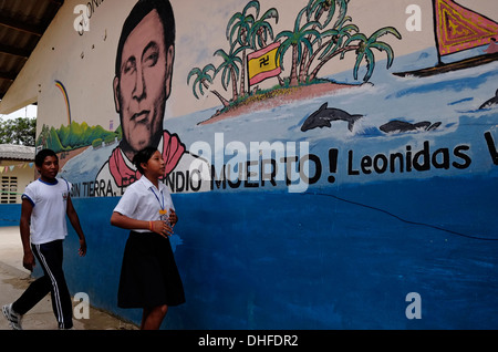 Schoolchildren from the Guna people walk past a painted wall depicting 1925 Kuna revolution leader Nele Kantule in Carti Sugtupu island village administered by Guna natives known as Kuna in the 'Comarca' (region) of the Guna Yala located in the archipelago of San Blas Blas islands in the Northeast of Panama facing the Caribbean Sea. Stock Photo
