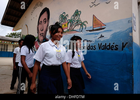 Schoolgirls from the Guna people walk past a painted wall depicting 1925 Kuna revolution leader Nele Kantule in Carti Sugtupu island village administered by Guna natives known as Kuna in the 'Comarca' (region) of the Guna Yala located in the archipelago of San Blas Blas islands in the Northeast of Panama facing the Caribbean Sea. Stock Photo