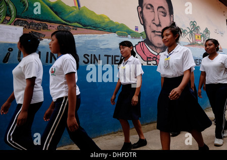 Schoolgirls from the Guna people walk past a painted wall depicting 1925 Kuna revolution leader Nele Kantule in Carti Sugtupu island village administered by Guna natives known as Kuna in the 'Comarca' (region) of the Guna Yala located in the archipelago of San Blas Blas islands in the Northeast of Panama facing the Caribbean Sea. Stock Photo