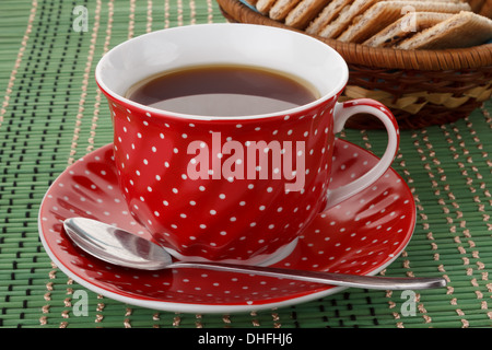 a polka dot mug sitting on a green placemat next to a basket of cookies Stock Photo