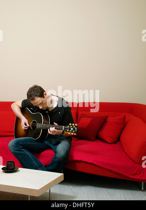 A man sitting on a sofa playing a Gibson guitar Stock Photo
