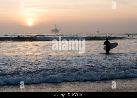 View of a California surfer silhouetted against the setting sun, with an off-shore platform visible in the distance. Stock Photo