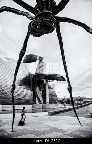 A woman walks below the large spider-like sculpture Maman by Louise Bourgeois next to the Guggenheim Museum in Bilbao, Spain. Stock Photo