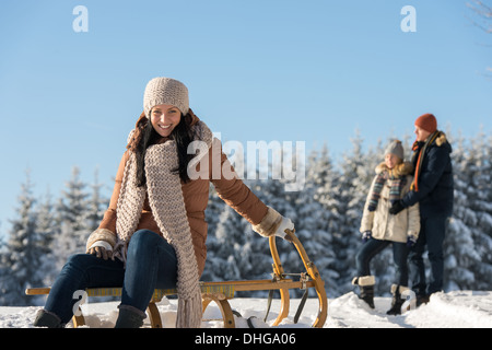 Young people enjoy sunny winter snow posing on wooden sledge Stock Photo