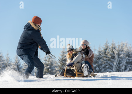 Young man pulling girls on winter sledge snow countryside Stock Photo