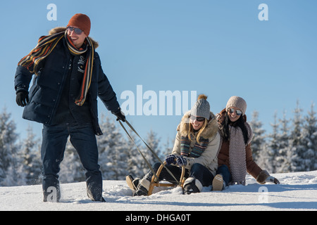 Young people enjoy sunny winter day sledge man pulling girlfriends Stock Photo