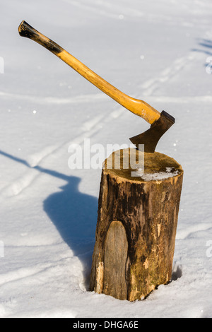 Ax stuck in wood log snow winter Stock Photo
