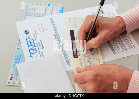 Senior woman pensioner writing a Nat West bank cheque to pay for a large oil fuel bill for home heating in Wales, UK, Britain Stock Photo