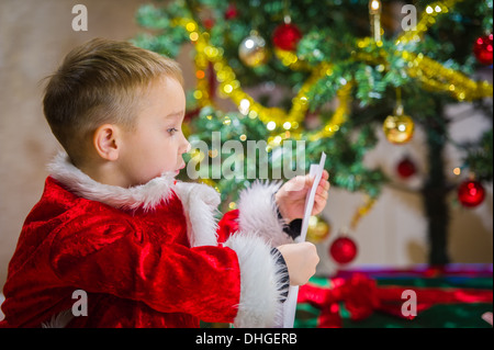 Adorable 5 year old boy check over him letter to Santa Claus, Christmas tree on background Stock Photo