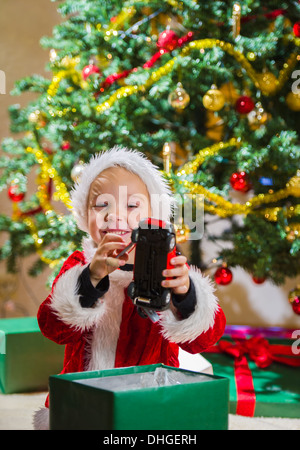 Surprised boy opens a Christmas gift, Christmas tree and gifts on background Stock Photo