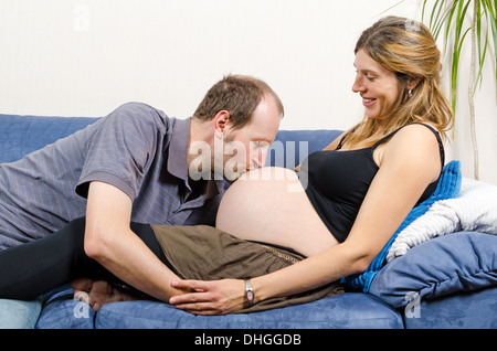 Happy man kissing tummy of happy pregnant woman sitting on couch Stock Photo