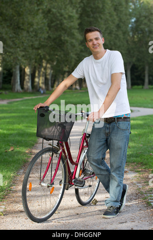 Young man standing next to his bike on a path in a park Stock Photo