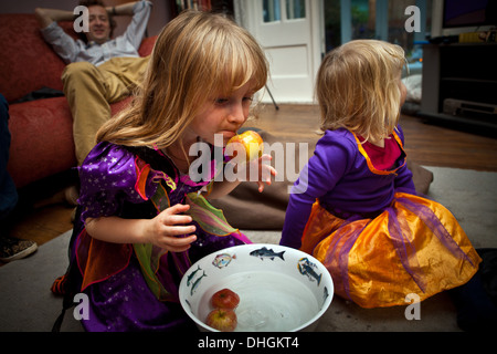 2 young sisters at home apple bobbing at Halloween with Dad in the background Stock Photo