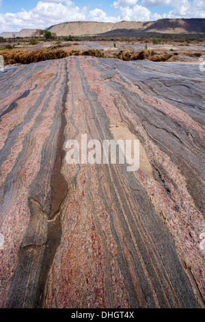 Banded precambrian rock at Lugard's falls in Tsavo East National Park with the distant escarpment of the Yatta Plateau Kenya Stock Photo