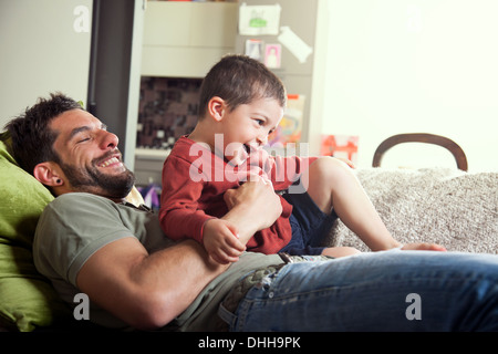 Father reclined on sofa with son on lap Stock Photo