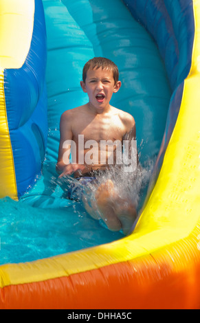 family water slide in back yard at home with water in summer and boy aged 10 playing and having fun Stock Photo