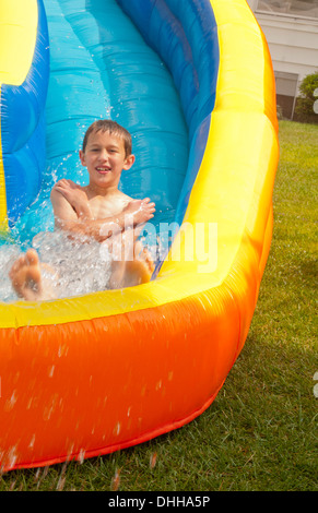 family water slide in back yard at home with water in summer and boy aged 10 playing and having fun Stock Photo