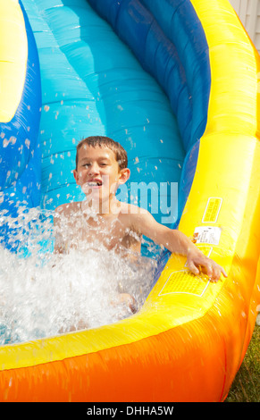 family water slide in back yard at home with water in summer and boy aged 10 playing and having fun Stock Photo